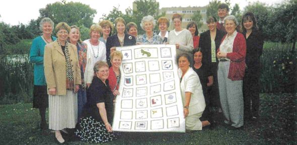 Catherine and colleagues presenting a handmade throw on the grass outside the Cavendish Laboratory