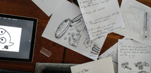 Top view of drawings, handwritten notes and a tablet on a desk
