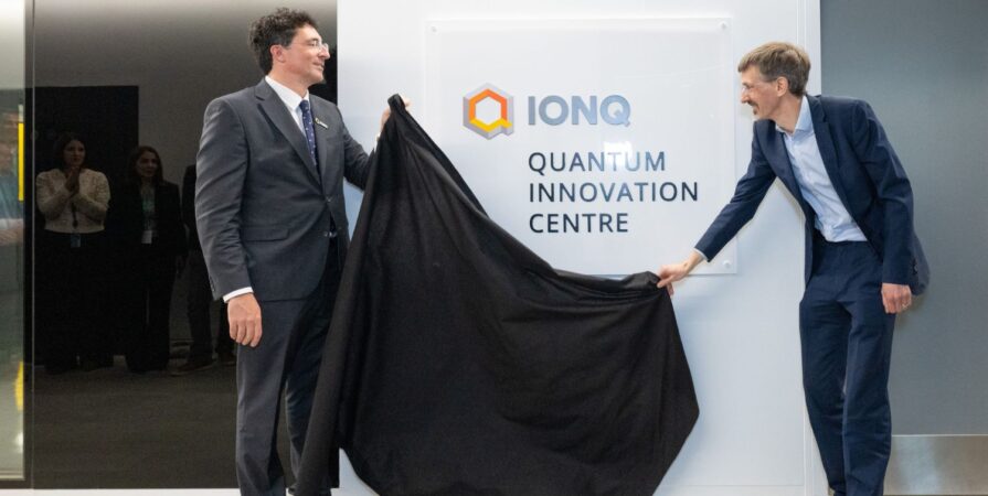 two men in suits remove a black curtain to unveil a sign that reads IonQ Quantum Innovation Centre