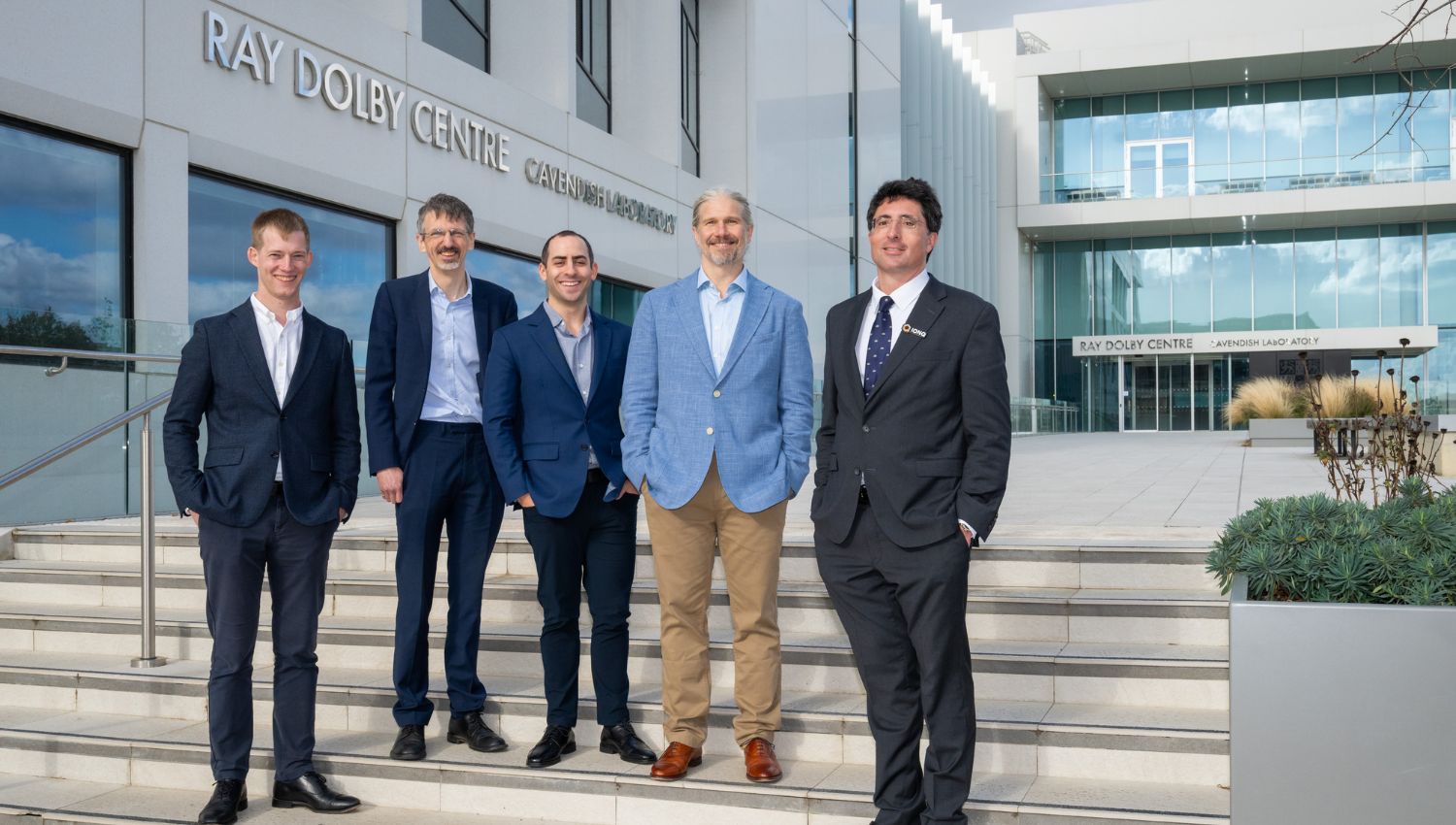 Five men in suits standing on stairs in front of a modern building