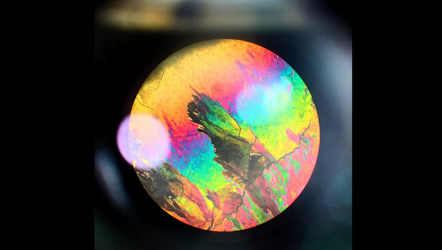 Small Made Big Observations of liquid crystals between crossed polarisers elegantly demonstrate how nanoscale differences in molecular orientation and interactions produce macroscopic functional and visual differences. Since they inhabit the phase space between an isotropic liquid and a highly ordered solid, behaviour at the macroscopic level is a direct, visible consequence of small-scale changes. When viewed through crossed polarisers, the discrete nature of the molecules and their alignment can be abstracted away, and we can view the liquid crystal system as a continuous medium with varying birefringent properties. Manipulation of the polarization of light provides the foundation for various technologies, most famously liquid crystal displays (LCDs). Here, nanoscale molecular orientation (small) is translated to visual information (big). This photo of the crystalline phase of 4-n-heptyloxybenzoic acid was taken through the eyepiece of a polarised optical microscope while characterising the phase diagram of the nOBA (4-n-alkoxybenzoic acid) homologues. In this series, the lower homologues (n = 1, 2) are non-mesogenic, while intermediate chains (n = 3 to 6) show nematic liquid crystal behaviour, and longer chains (n ≥ 7) additionally exhibit smectic phases. The image doubly captures this year's theme "Big and Small". We observe the "small" microscale sample section that has been magnified, revealing the "big" visual display. Equally, the "big" patterns that we see directly result from the "small" nanoscale molecular interactions and alignment.